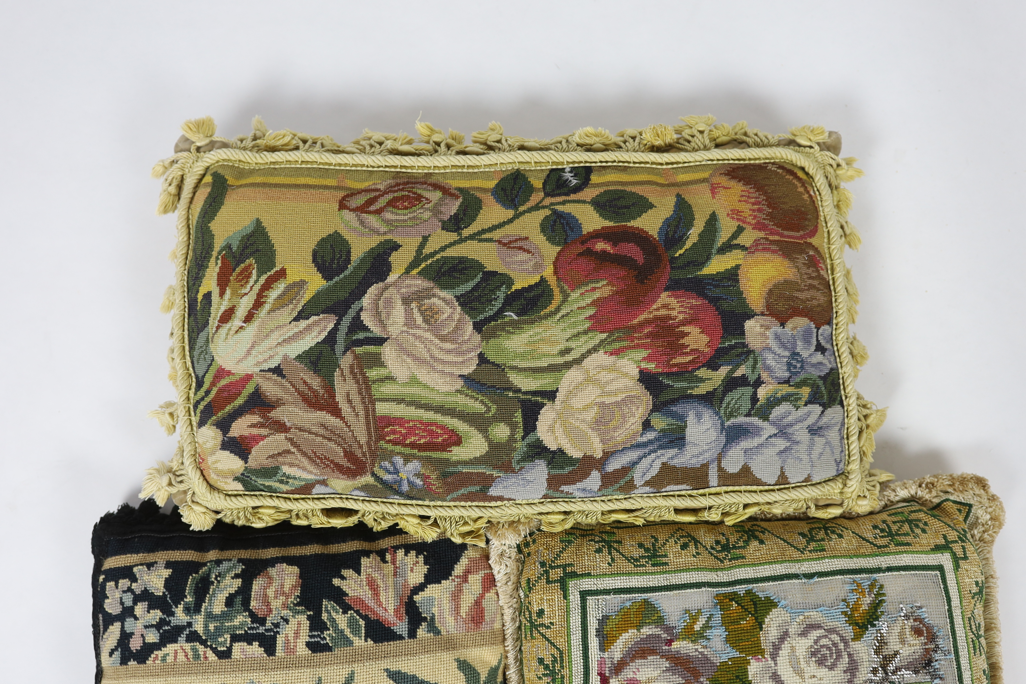 A Victorian Berlin beadwork floral cushion, 43cm wide, 41cm high, together with two similar 20th century wool worked cushions, all edged with tasselling and braiding